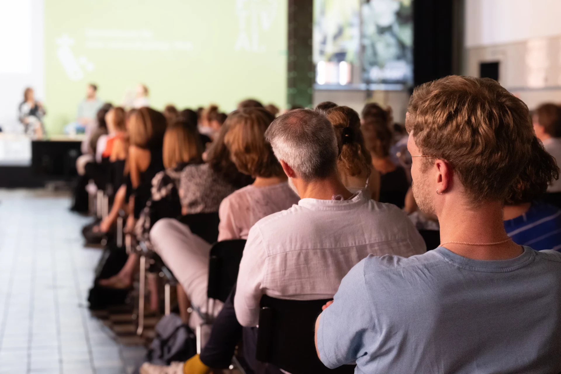 Blick von hinten auf Publikum und Zuschauer:innen einer Konferenz