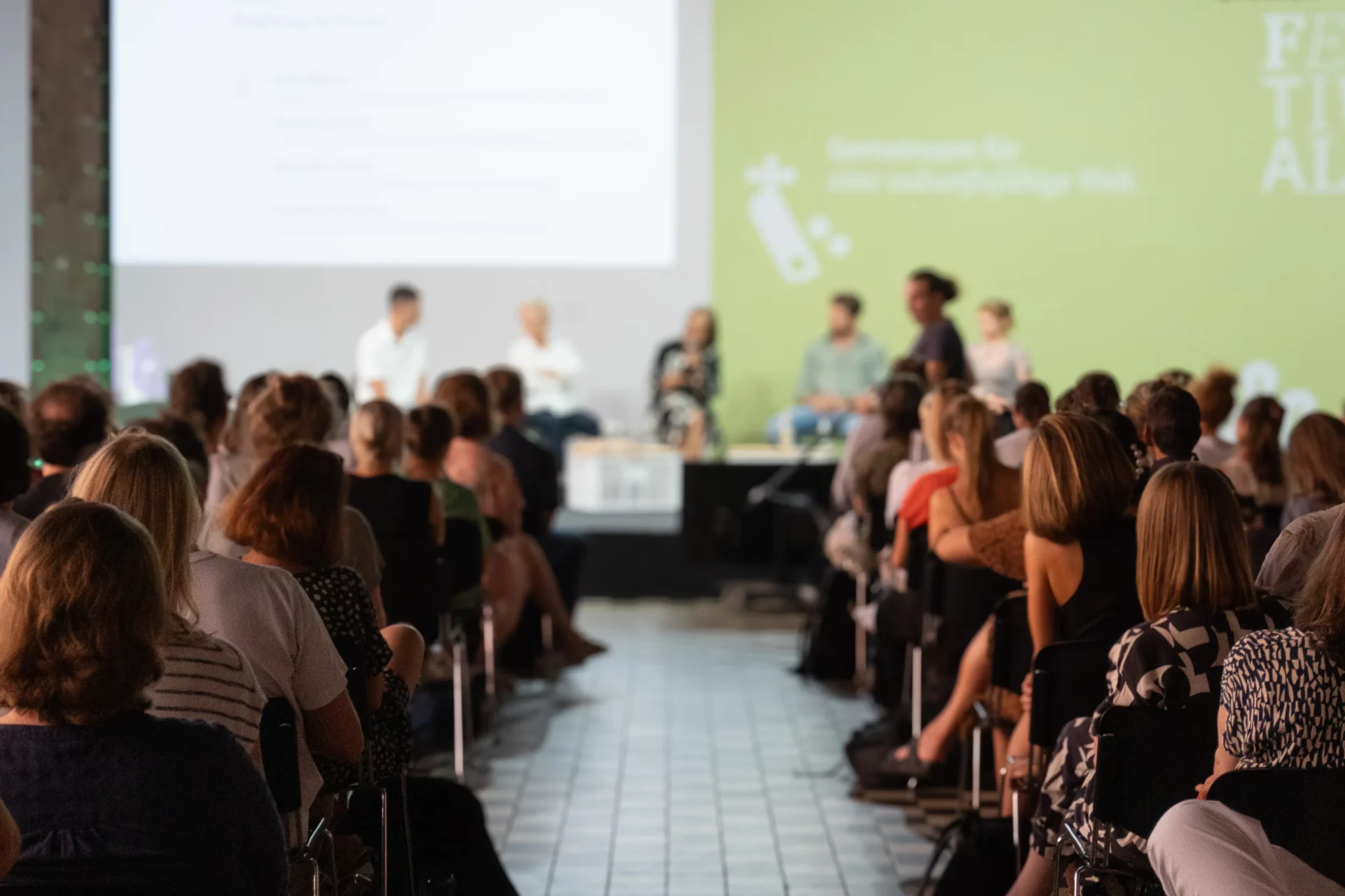 Blick von hinten auf Publikum und Bühne einer Konferenz