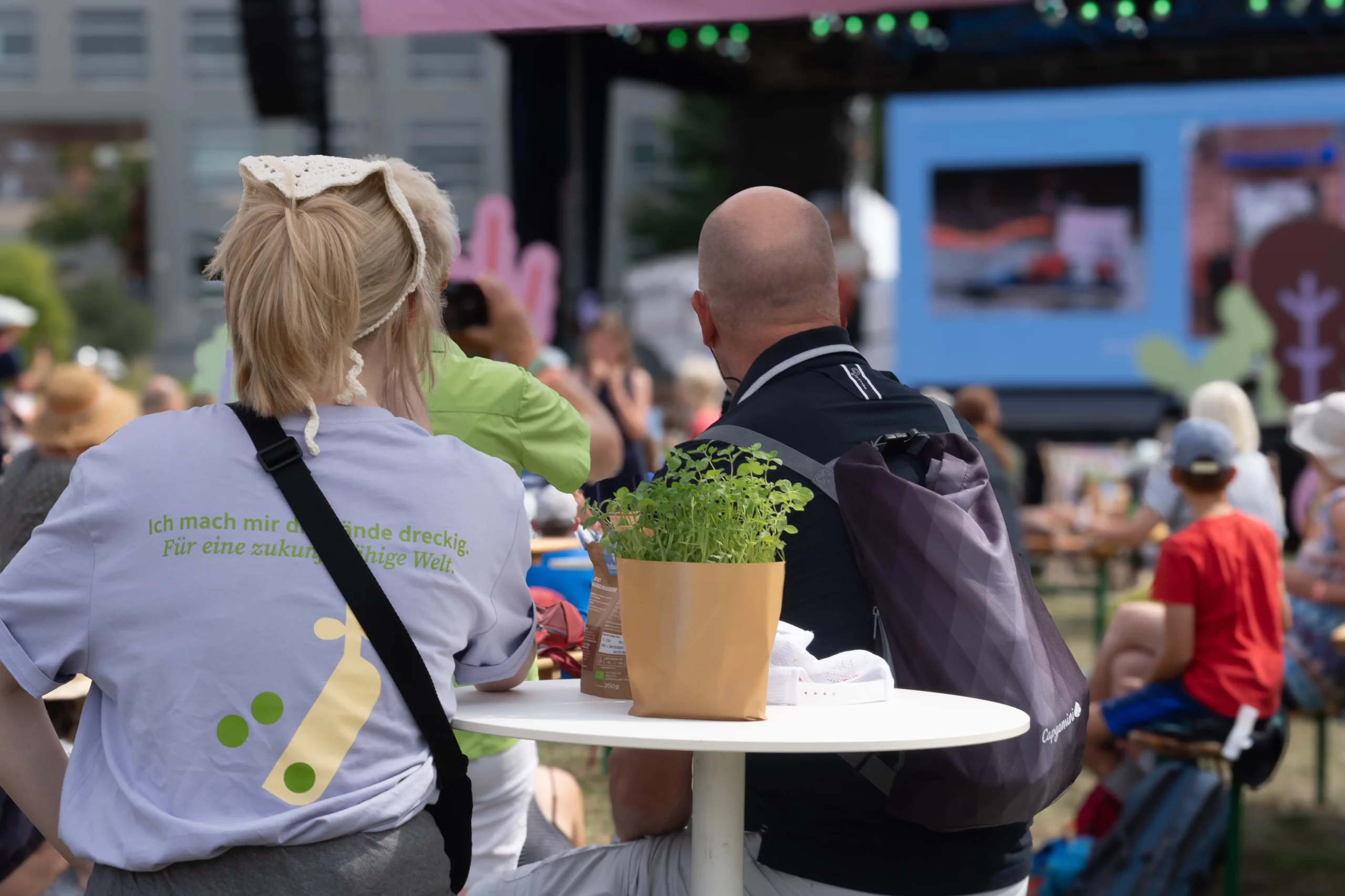 Menschen schauen auf Bühne mit Redner:innen, Bühne ist draußen