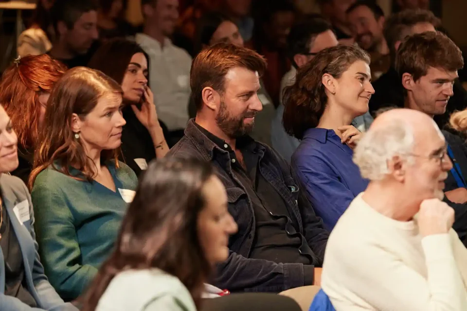 Publikum in einer Konferenz, der Fokus liegt auf zwei Personen die angeregt zuhören.