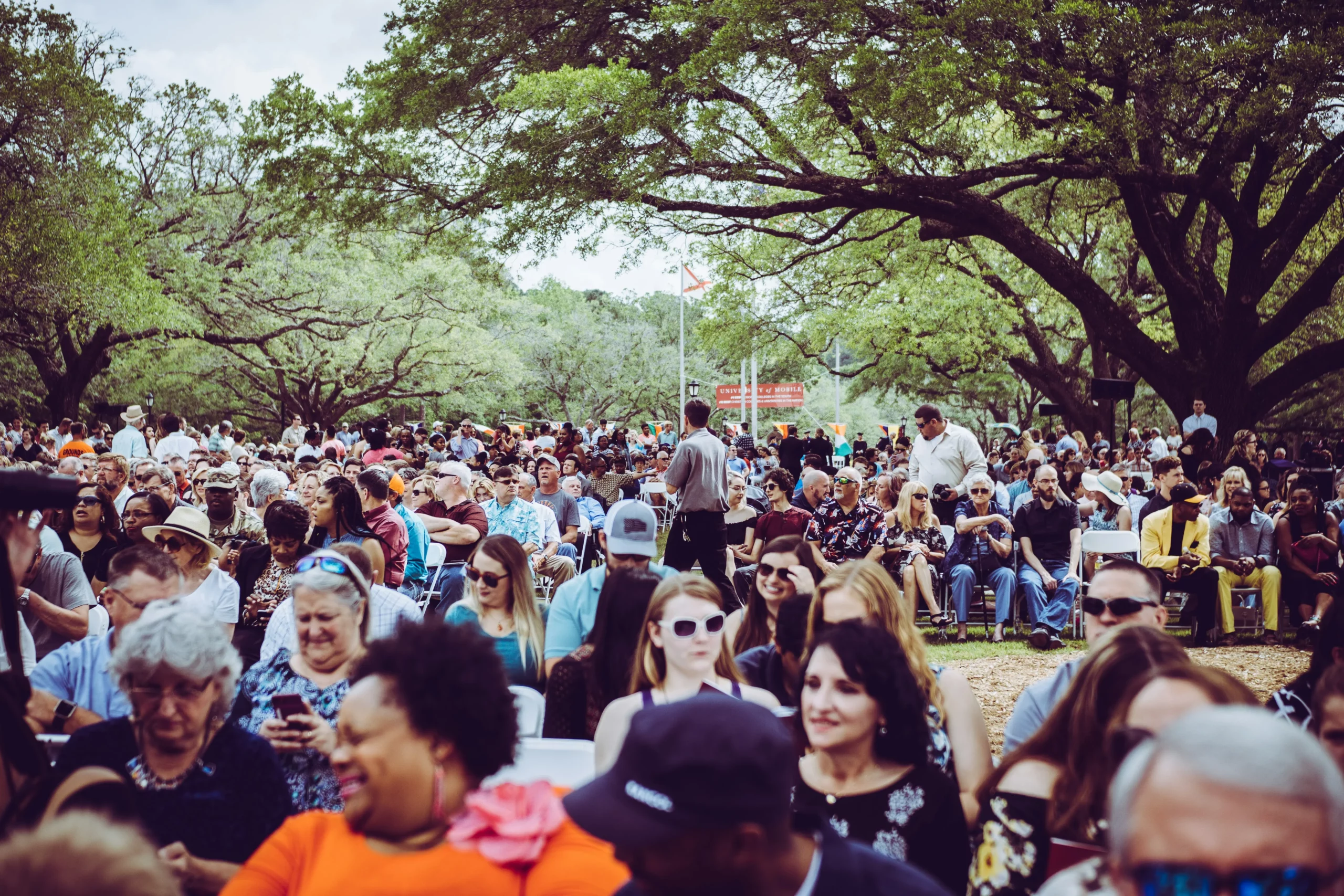 Viele Menschen sitzen auf Stühlen und schauen in eine Richtung in der einem Park. Konzert, Konferenz im Freien