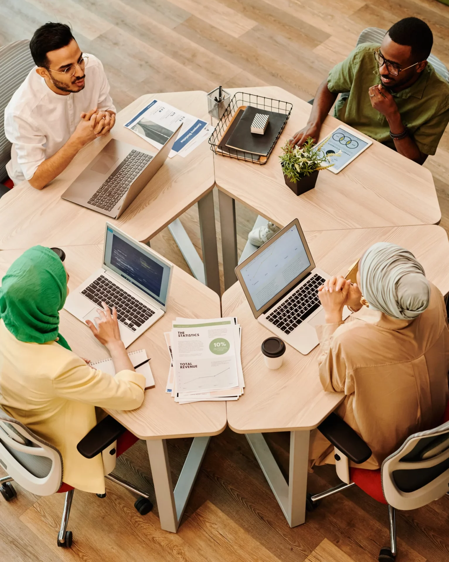 4 Junge Menschen sitzen im Kreis an Tischen vor ihren PCs und besprechen sich.