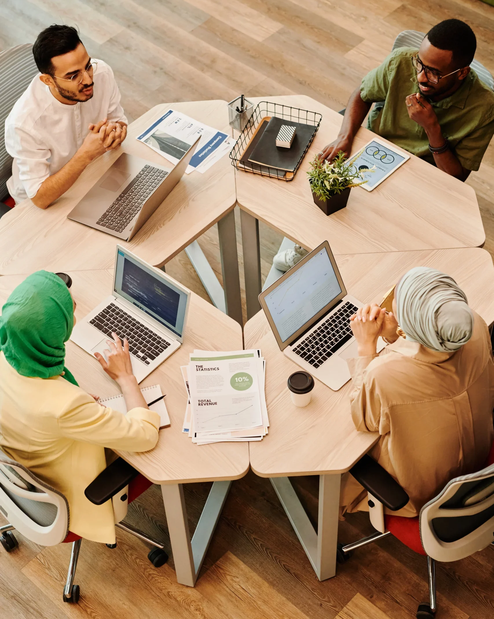 4 Junge Menschen sitzen im Kreis an Tischen vor ihren PCs und besprechen sich.